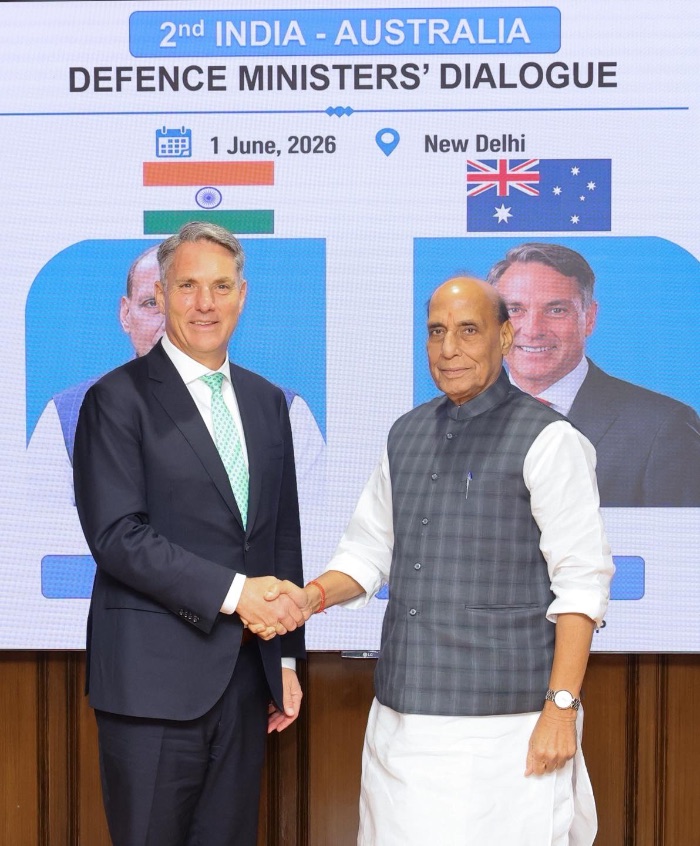 a man in suit and a man in traditional indian dress shake hands