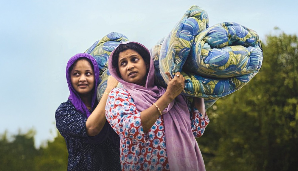 a film still showing two women carrying a cotton mattress